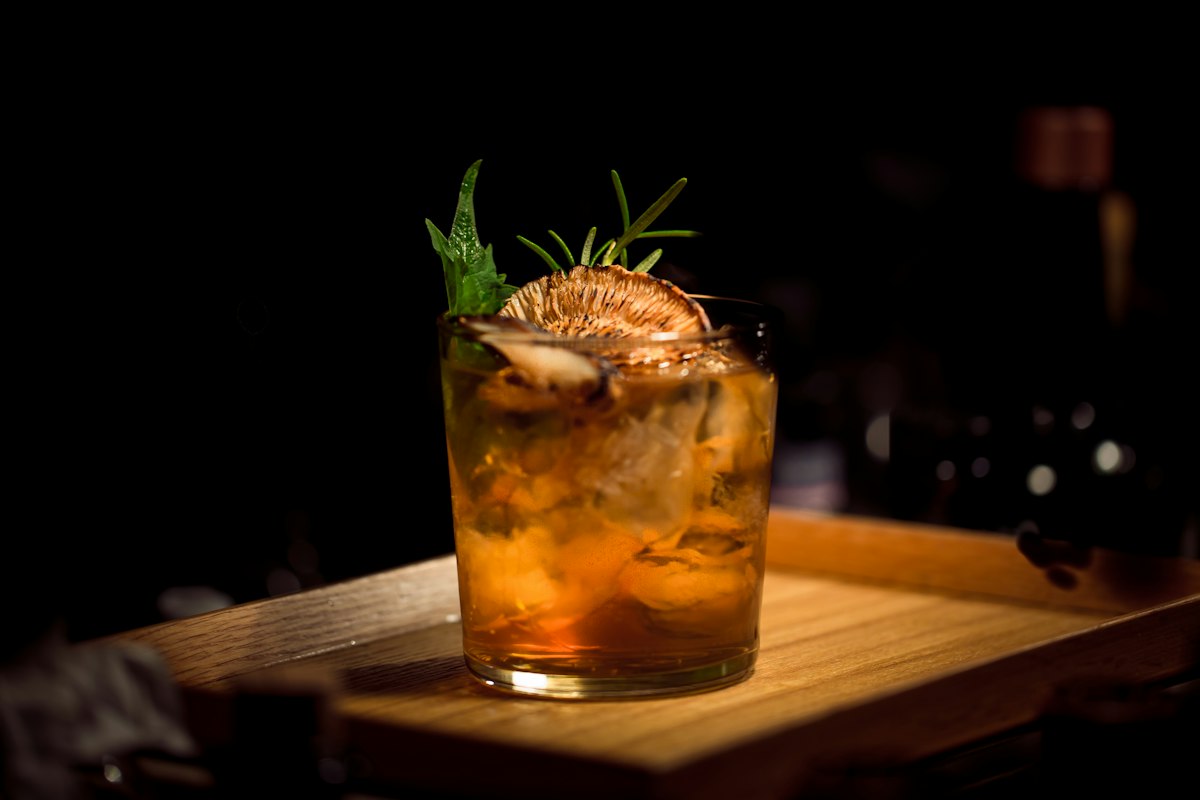 An Old Fashioned cocktail with a charred citrus wheel and herb garnish